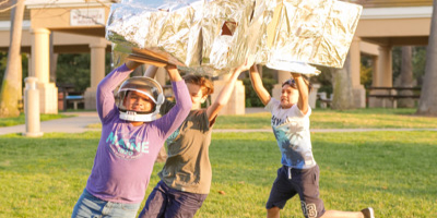 three children running outside with a homemade rocket